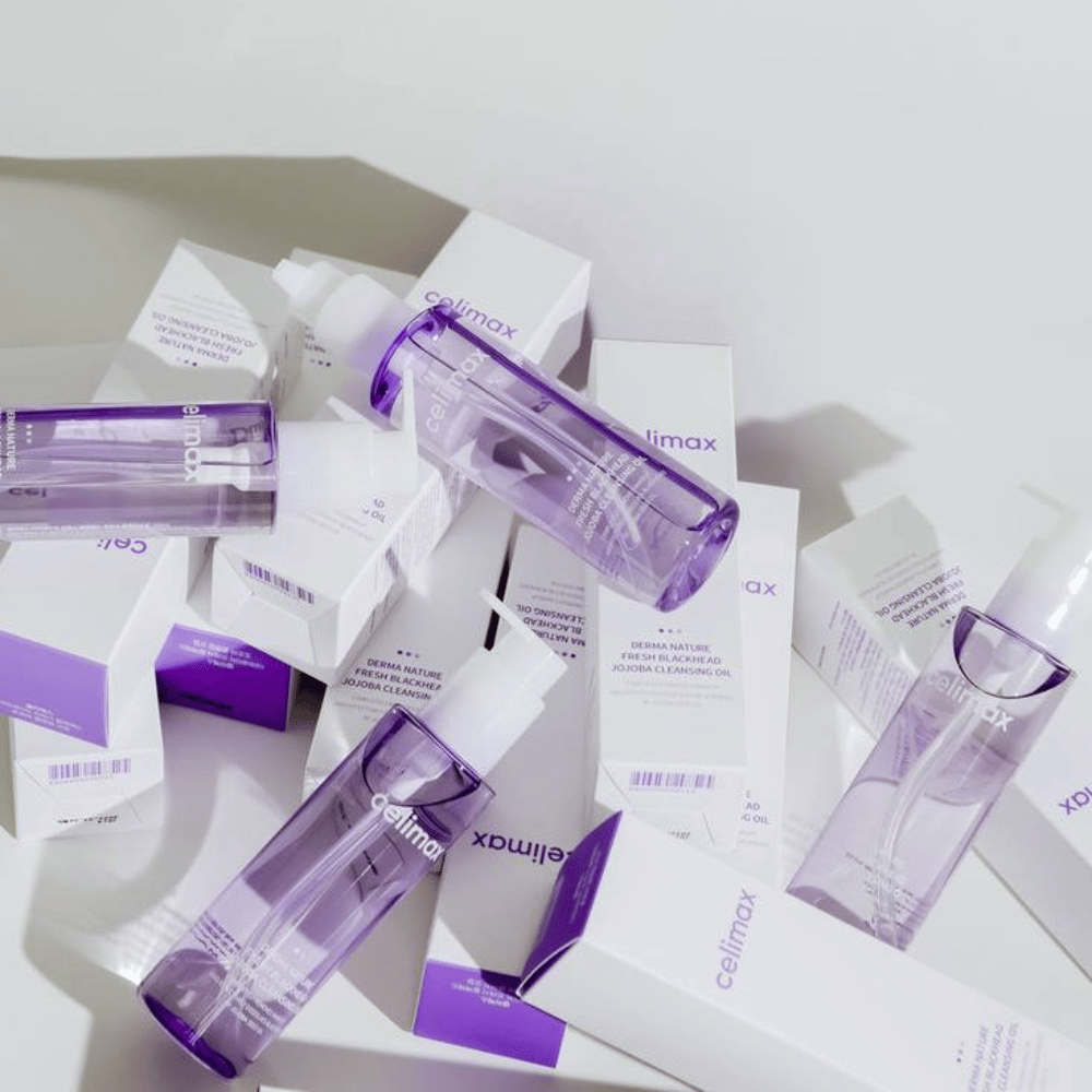 Celimax Derma Nature Fresh Blackhead Jojoba Cleansing Oil in bottiglie viola posizionate tra confezioni di prodotti bianchi con dettagli viola.
