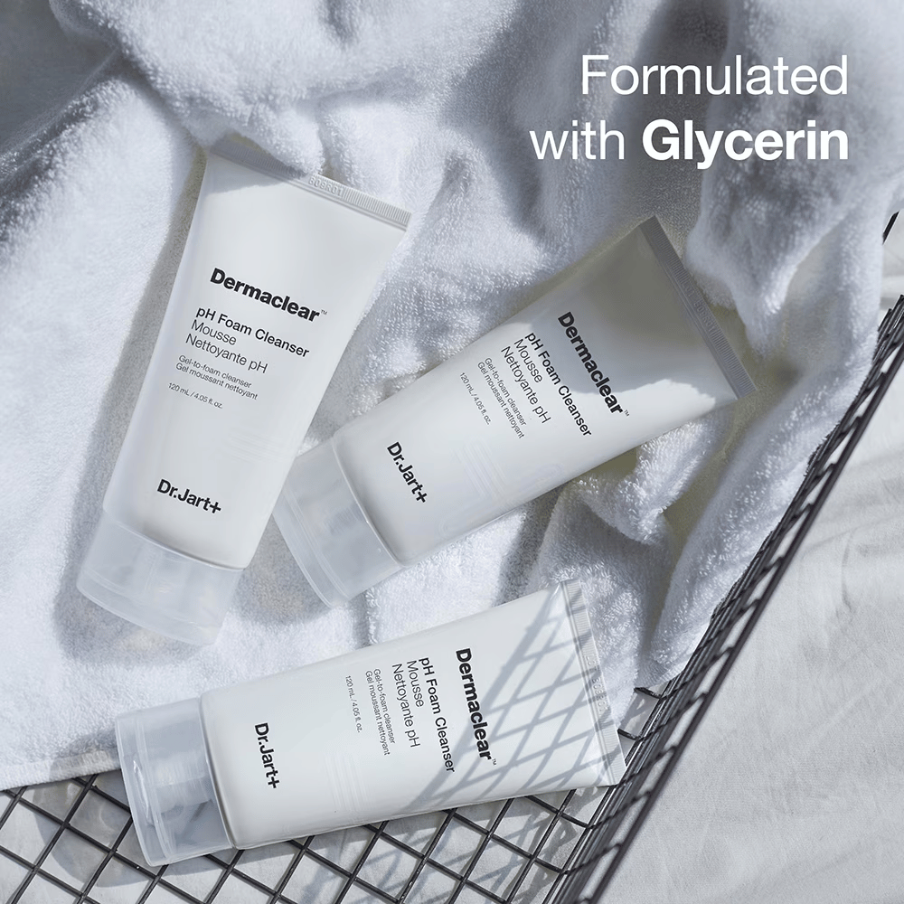 Tre tubi di Dr.Jart+ Dermaclear pH Foam Cleanser su un asciugamano di spugna bianco in un cestino di metallo, con la scritta "Formulated with Glycerin" nell'angolo superiore.