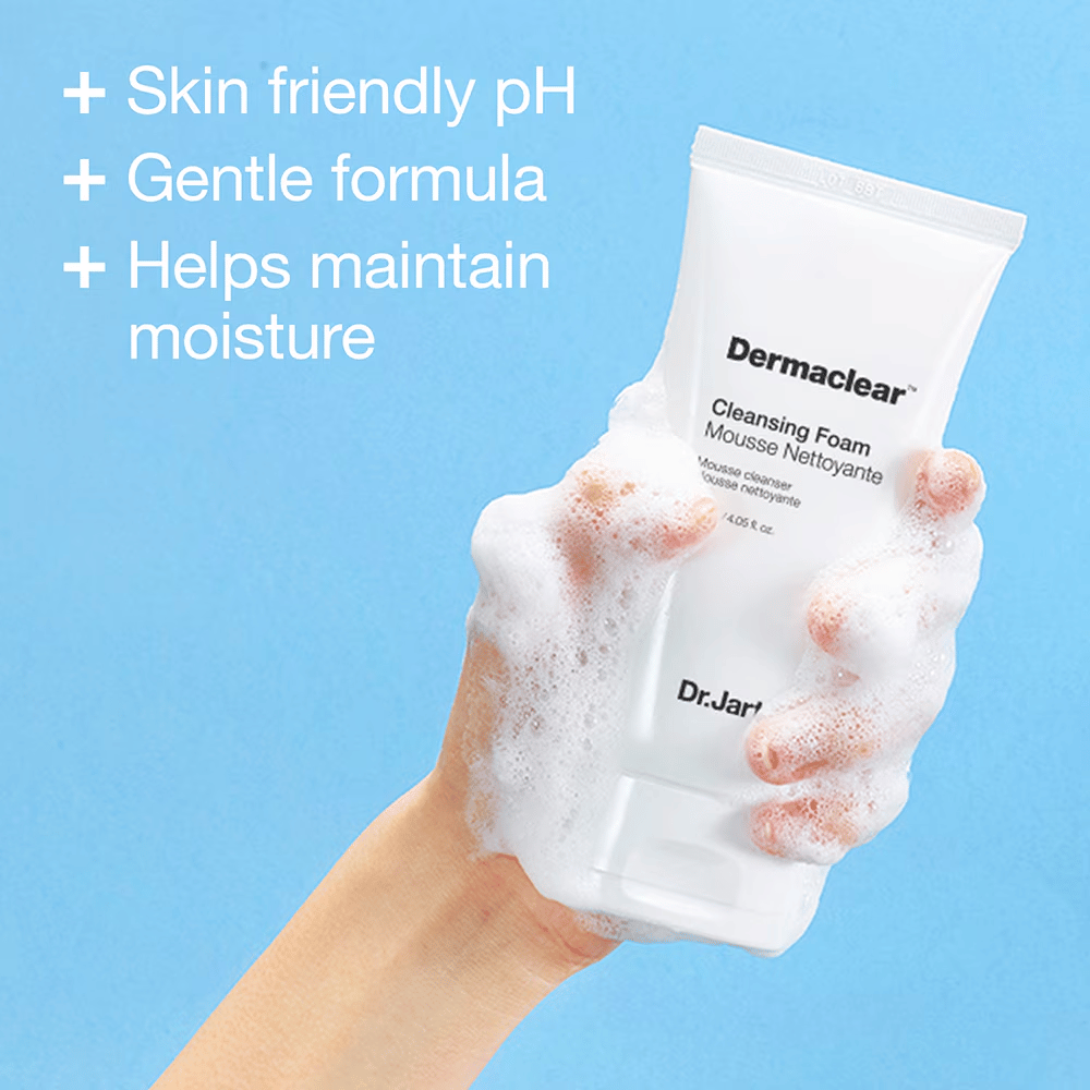 Mano coperta di schiuma tiene Dr.Jart+ Dermaclear Cleansing Foam su sfondo blu, con testo che evidenzia pH amico della pelle, formula delicata e proprietà idratanti.