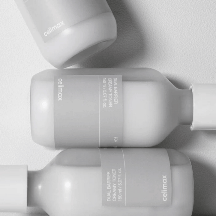 Tre liggande flaskor av Celimax Dual Barrier Creamy Toner i en minimalistisk design med grå etikett och mjukt ljus – perfekt för känslig och torr hud.