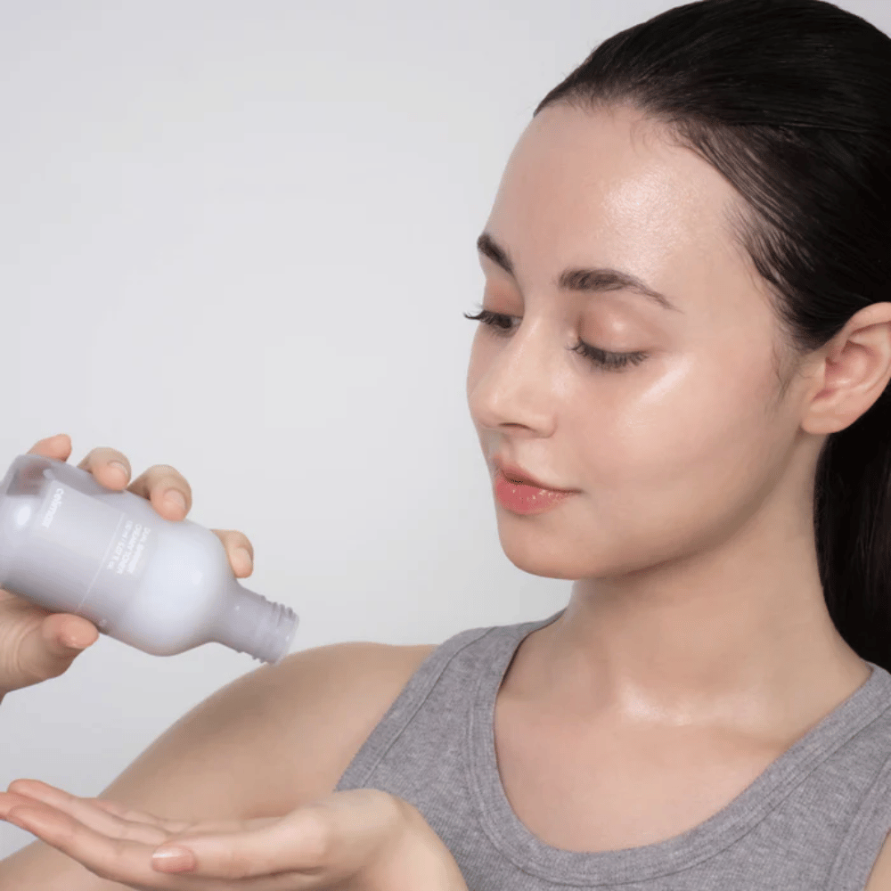 Donna con pelle lucida e idratata applica Celimax Dual Barrier Creamy Toner versando il prodotto nel palmo della mano prima della sua routine di cura della pelle.