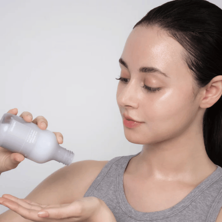 Kvinna med glansig, återfuktad hud applicerar Celimax Dual Barrier Creamy Toner genom att hälla produkten i handflatan inför sin hudvårdsrutin.