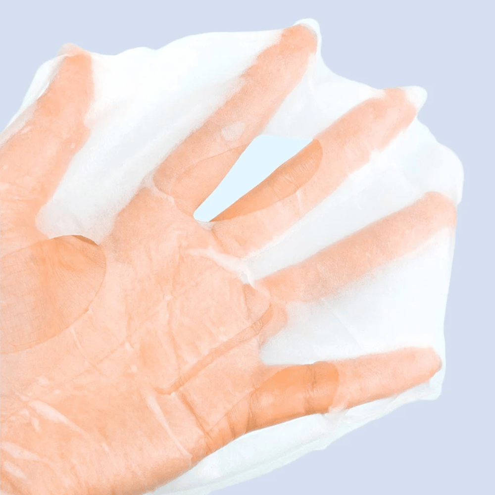 Una maschera viso trasparente e umida viene tenuta su una mano contro uno sfondo azzurro chiaro. La maschera è progettata per coprire il viso con spazi per occhi e bocca.