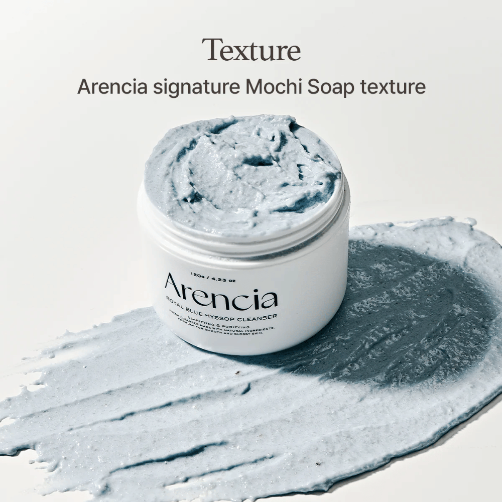 Barattolo aperto con Arencia Fresh Blue Hyssop Rice Mochi Cleanser, posizionato sopra uno strato spalmato della formula detergente blu e cremosa che mostra la sua consistenza simile al mochi.