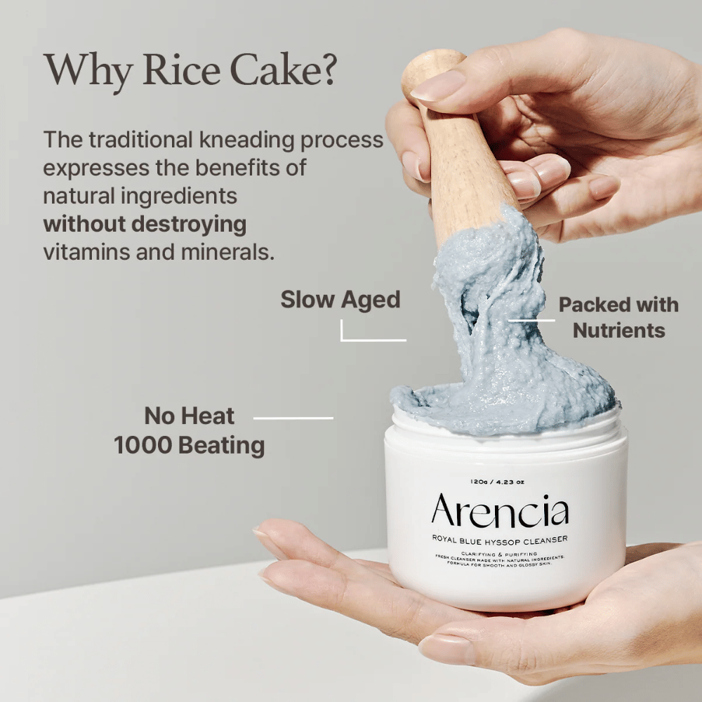 Mano che tiene il barattolo detergente "Arencia Royal Blue Hyssop Cleanser" con un cucchiaio di legno che solleva la pasta detergente blu, simile al mochi. Il testo nell'immagine descrive i benefici del processo di lavorazione del riso, come "No Heat", "1000 Beating", "Slow Aged" e "Packed with Nutrients".