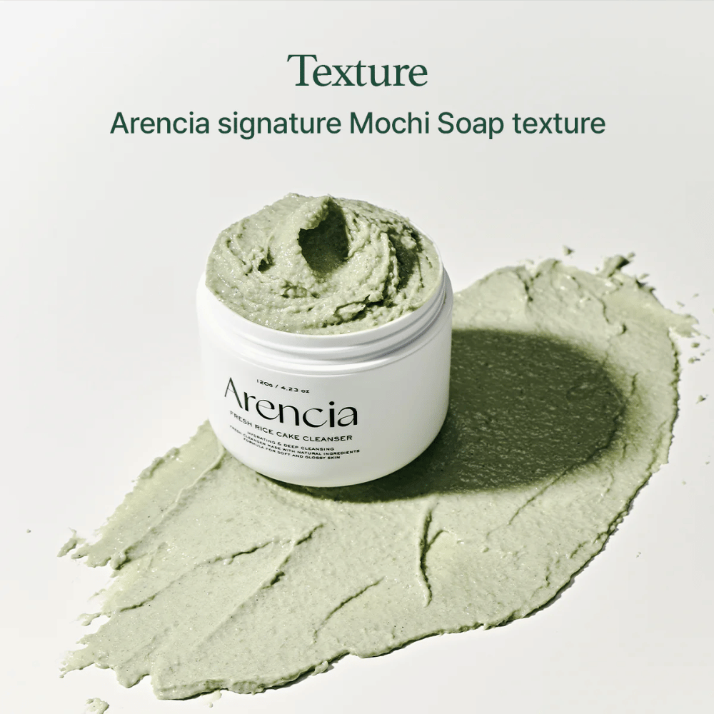 Arencia Fresh Rice Cake Cleanser in barattolo aperto con una texture cremosa verde simile al mochi sparsa intorno al barattolo su una superficie bianca.