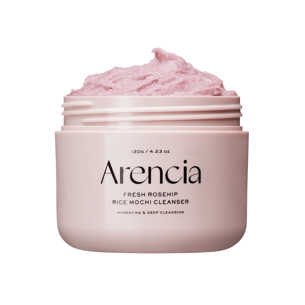 Primo piano di un barattolo rosa con Arencia Royal Rosehip Cleanser, pieno di crema detergente rosa con una texture simile a mochi montata. Il testo sul barattolo indica che il prodotto idrata e deterge in profondità.