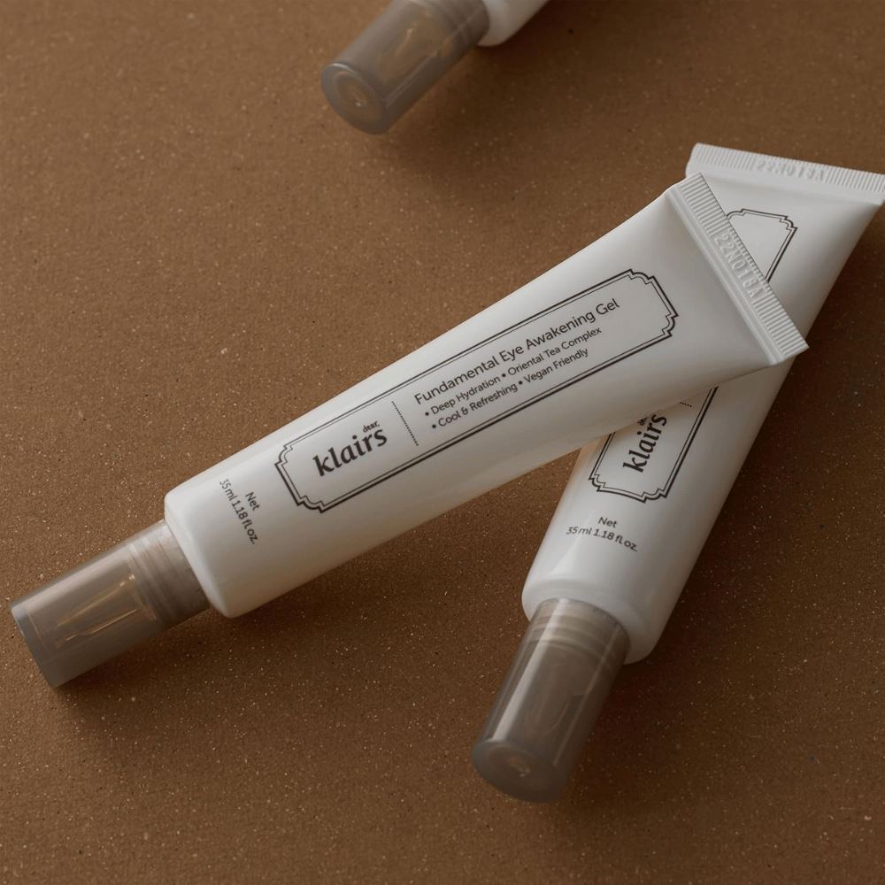Immagine lifestyle con due tubi di Klairs Fundamental Eye Awakening Gel posizionati su uno sfondo marrone caldo. La composizione mette in risalto il design elegante del prodotto e la sua sensazione premium, mantenendo al contempo il focus sulla cura del contorno occhi e sull’idratazione.