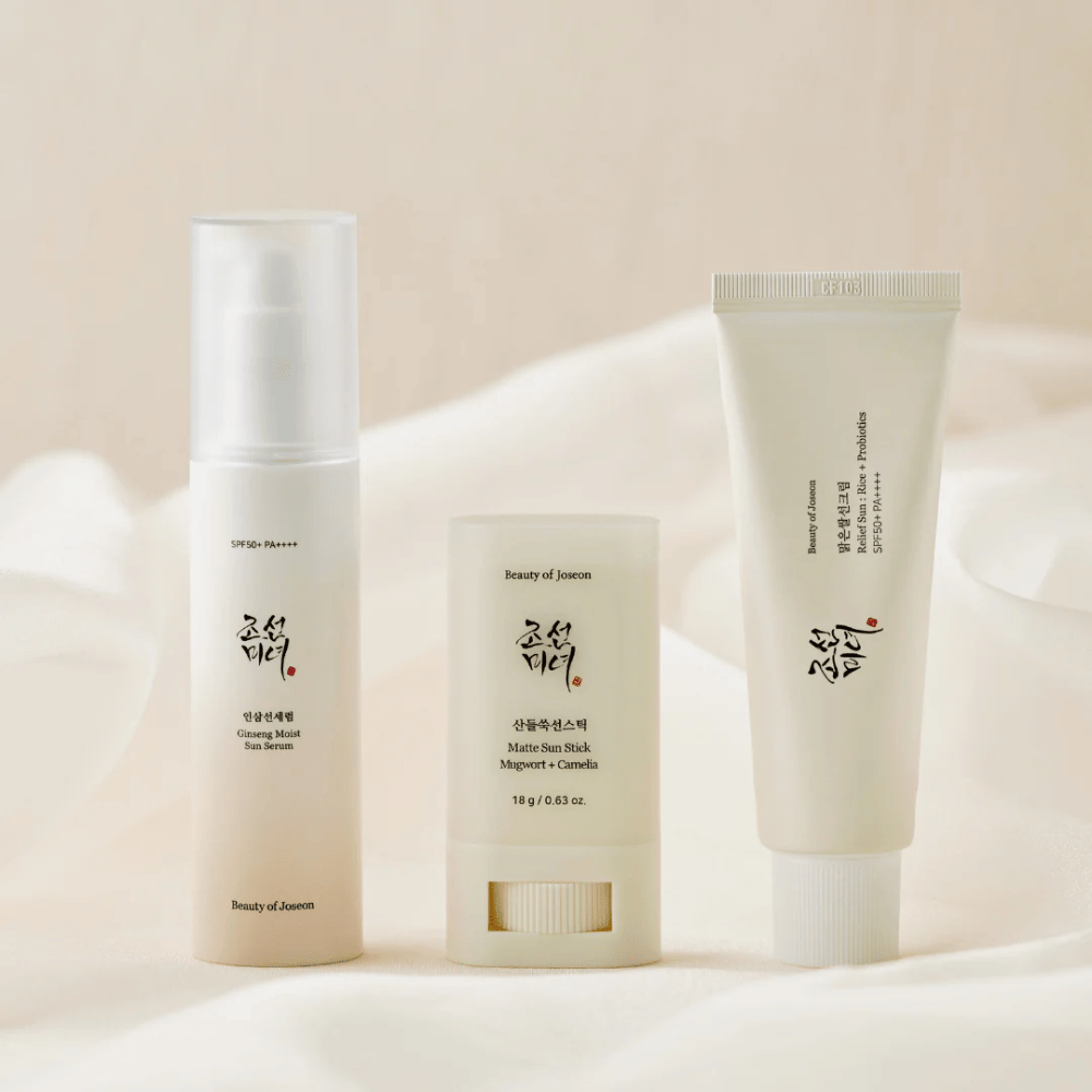 Tre prodotti solari da Beauty of Joseon – Ginseng Moist Sun Serum, Matte Sun Stick e Relief Sun Rice + Probiotics – sono allineati su un tessuto color crema con luce soffusa.