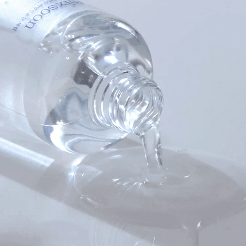 Primo piano di siero trasparente versato da una bottiglia Mixsoon Glacier Water Hyaluronic Acid Serum su una superficie lucida.