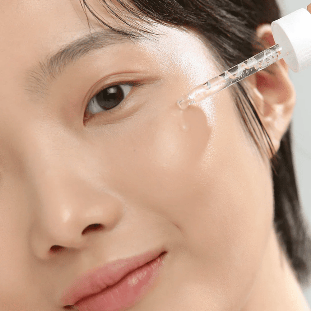 Primo piano di una donna che applica il siero sulla guancia con una pipetta – cura della pelle che dona luminosità e idratazione.