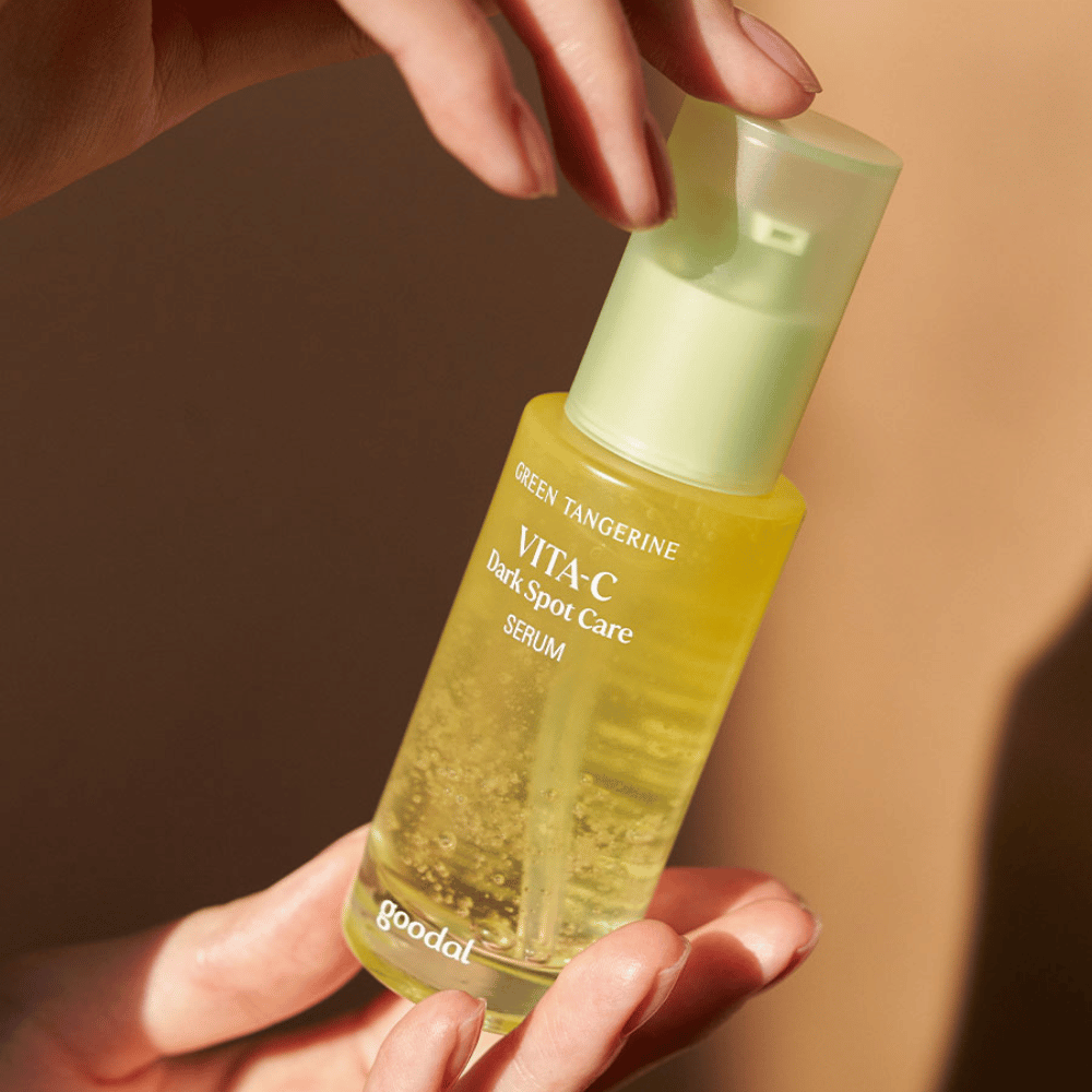 Una persona che tiene in mano una bottiglia Green Tangerine Vita C Dark Spot Care Serum 40ml da Goodal per l'iperpigmentazione e la cura delle macchie scure.