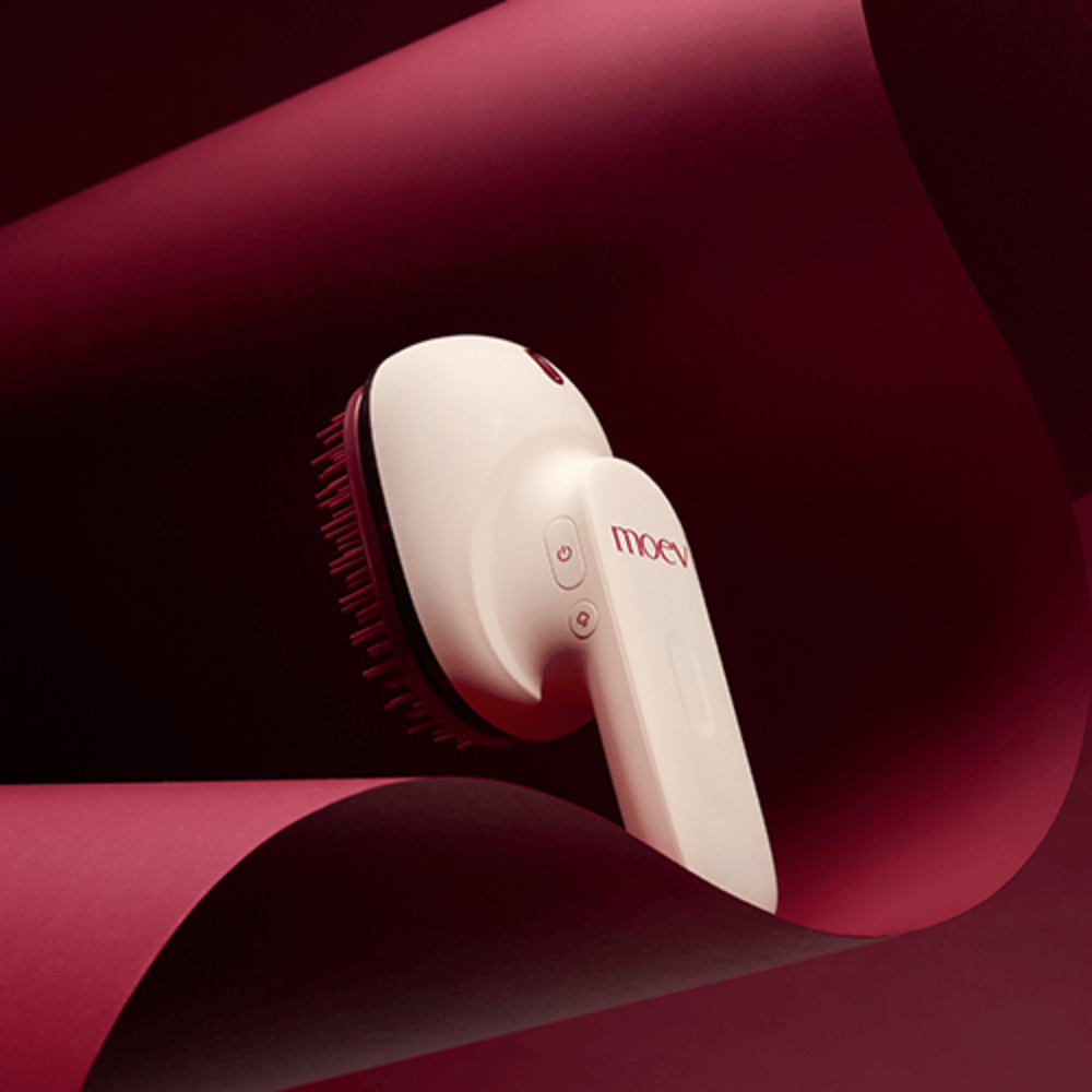 MOEV Hair Steamer Pro in design elegante su sfondo rosso. Spazzola innovativa per la cura dei capelli che utilizza vapore e calore per dare lucentezza, morbidezza e salute dei capelli rafforzata.