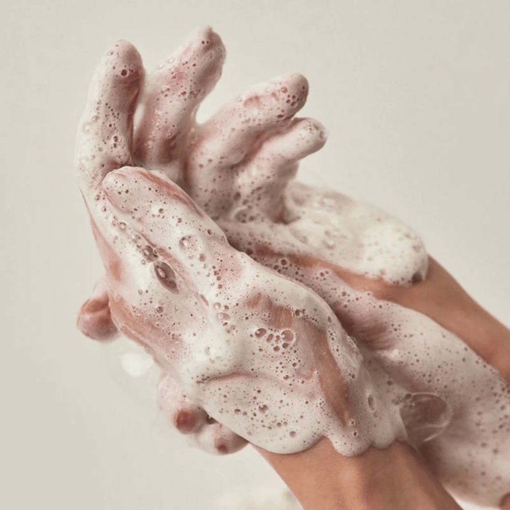 Primo piano di mani coperte da una ricca e cremosa schiuma detergente. L'immagine illustra la schiuma e le proprietà detergenti del prodotto, trasmettendo chiaramente il senso d'uso e della texture.