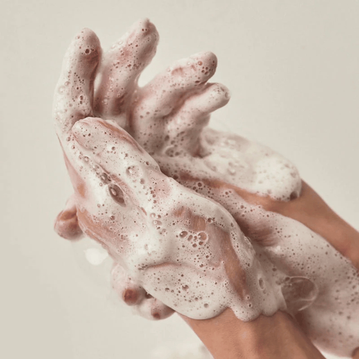 Primo piano di mani coperte da una ricca e cremosa schiuma detergente. L'immagine illustra la schiuma e le proprietà detergenti del prodotto, trasmettendo chiaramente il senso d'uso e della texture.