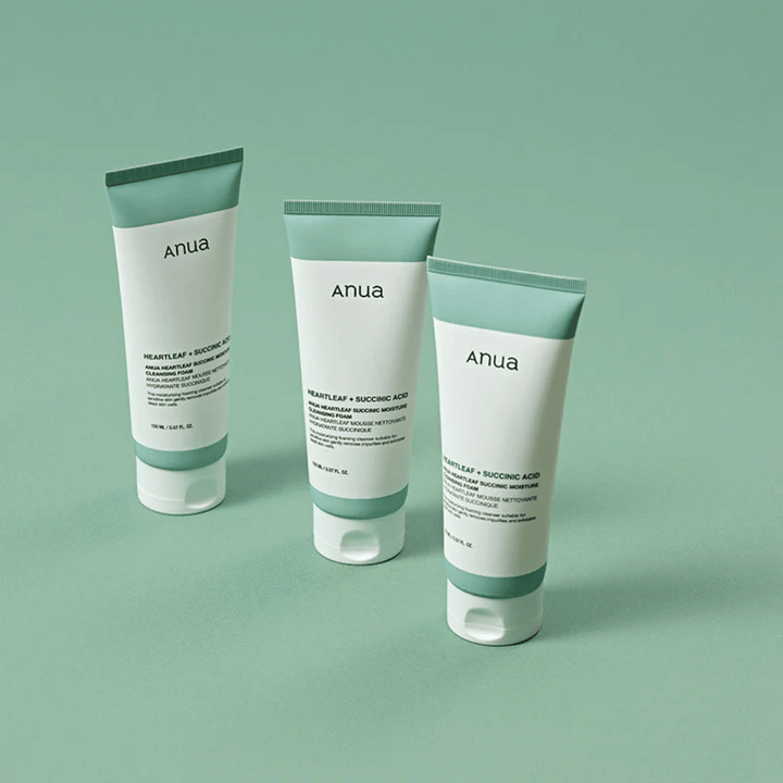 Tre confezioni di Anua Heartleaf + Succinic Acid Moisture Cleansing Foam presentate su uno sfondo verde chiaro. L'immagine evidenzia il design pulito e minimalista del prodotto e trasmette un'impressione professionale della linea di prodotti.