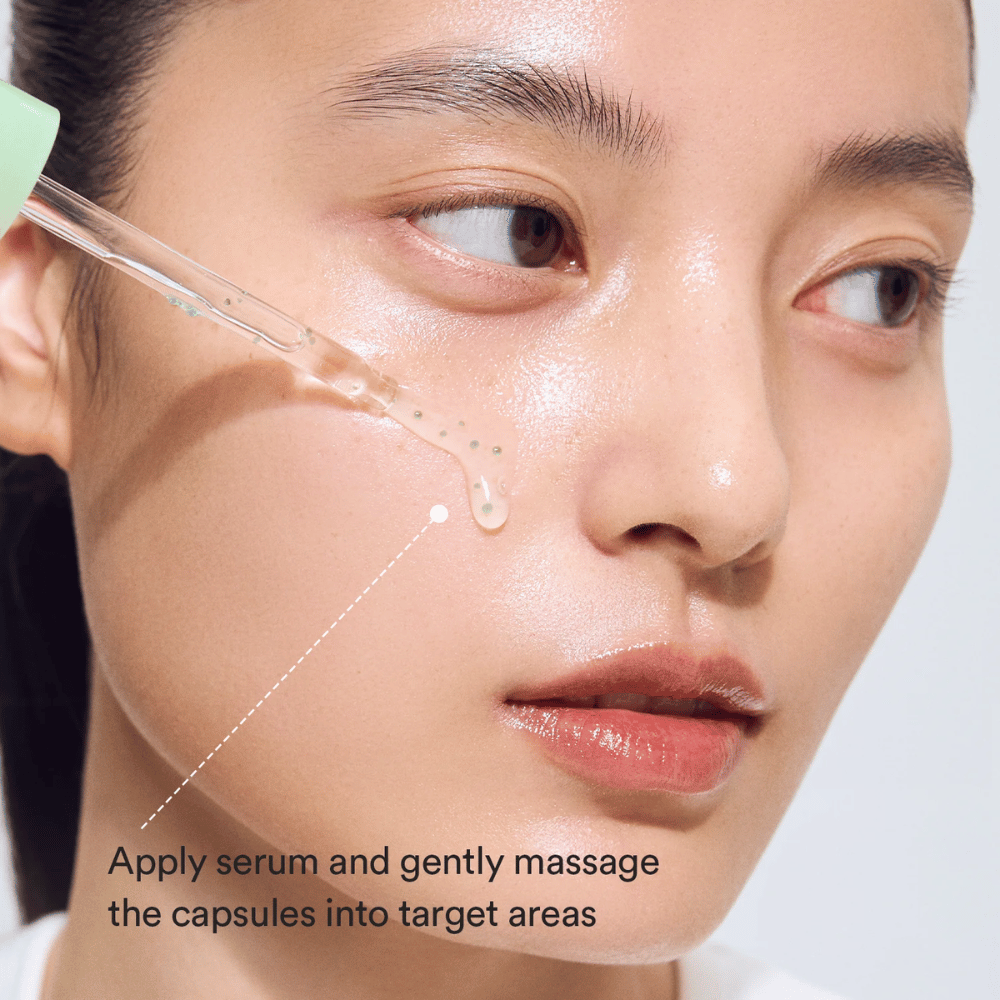 Primo piano di una modella che applica il siero con il contagocce mentre le capsule verdi vengono massaggiate nella pelle per un effetto lenitivo e idratante.