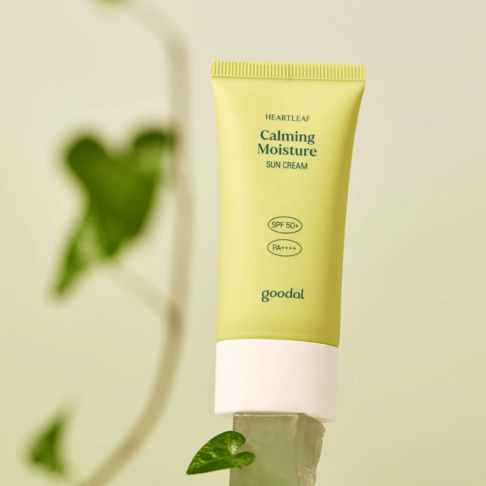 Goodal Heartleaf Calming Moisture Sun Cream SPF50+ PA++++ posizionata su una lastra di vetro con pianta verde sullo sfondo - una crema solare lenitiva per pelle sensibile.