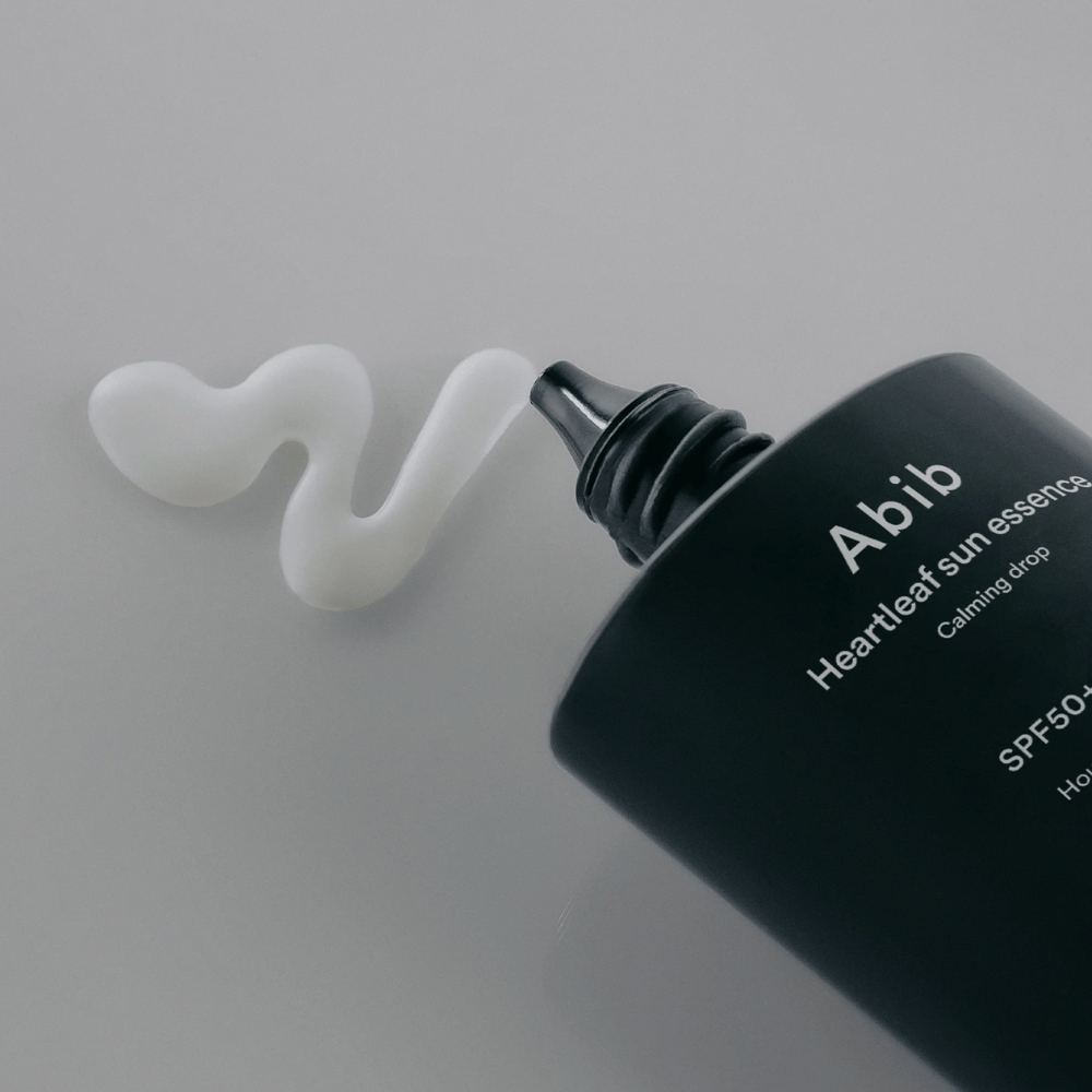 Primo piano su Abib Heartleaf Sun Essence Calming Drop con la crema solare spremuta in una linea bianca e ondulata su una superficie chiara.
