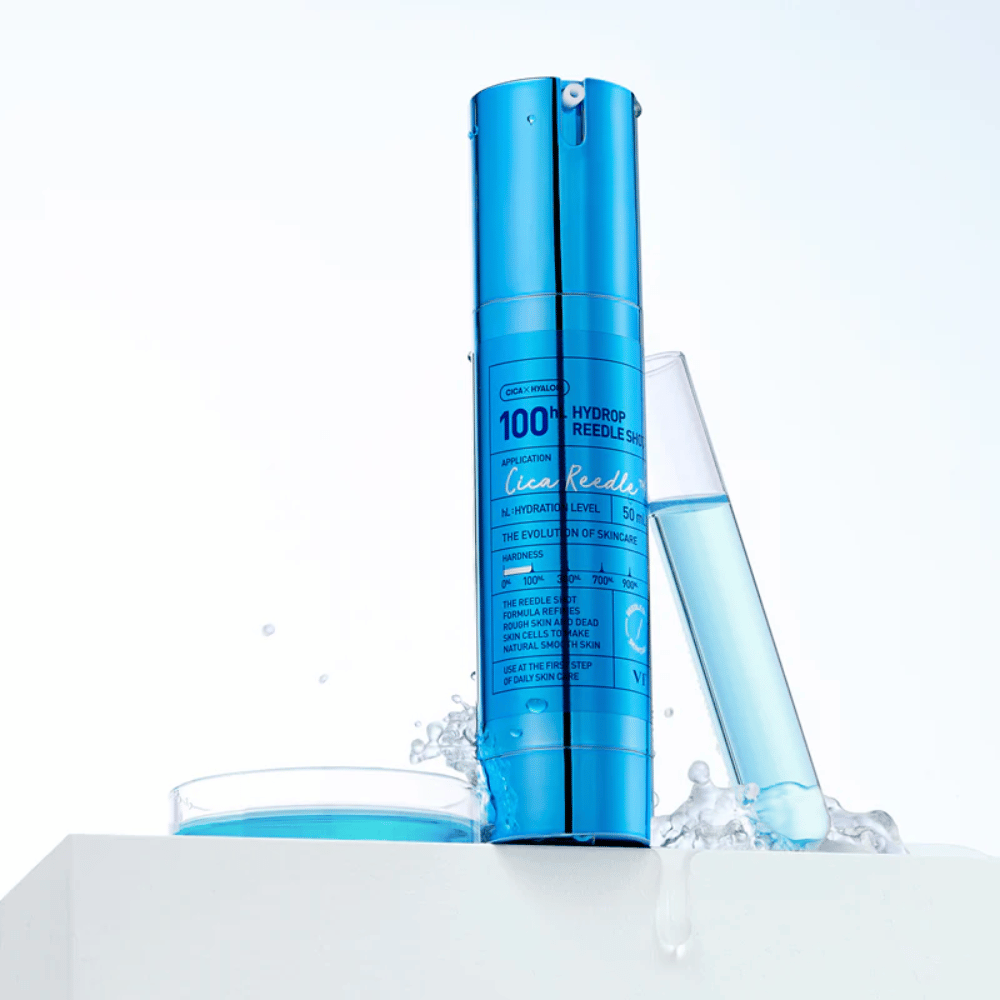 Bottiglia blu VT Cica Hyalon Hydrop Reedle Shot 100hL in piedi su superficie bianca con schizzi d'acqua, accanto a una provetta piena di liquido blu e un tappo rotondo con lo stesso liquido.