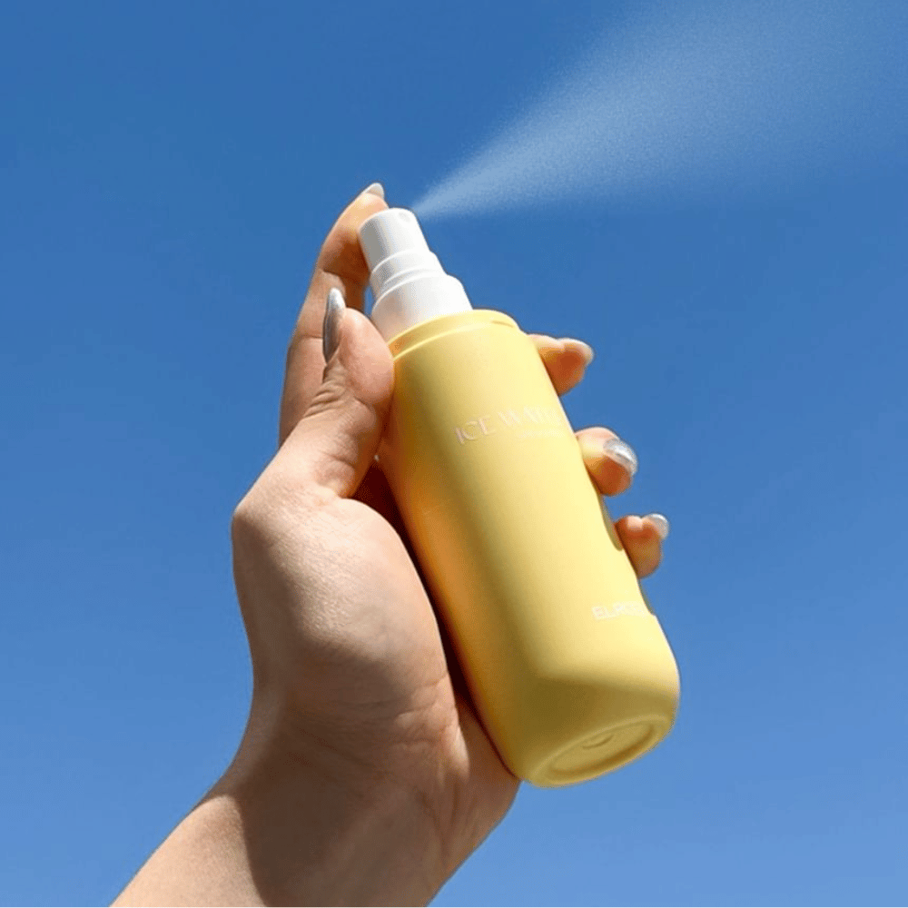 ELROEL Ice Water Sun Mist SPF 40 PA+++ mist solare spruzzata dal flacone verso il cielo azzurro, protezione solare leggera che idrata e rinfresca la pelle