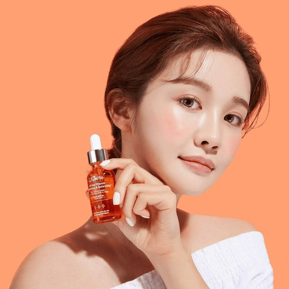 Una donna che tiene in mano una bottiglia di JUMISO All Day Vitamin Brightening & Balancing Facial Serum 30ml.