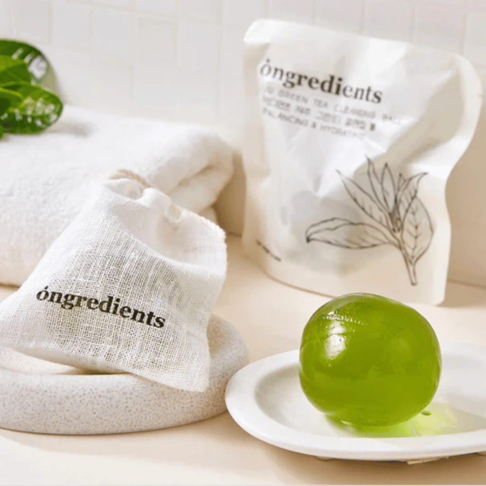 Óngredients Jeju Green Tea Cleansing Ball posizionato su un piatto con confezione e asciugamano – detergente delicato con tè verde di Jeju.