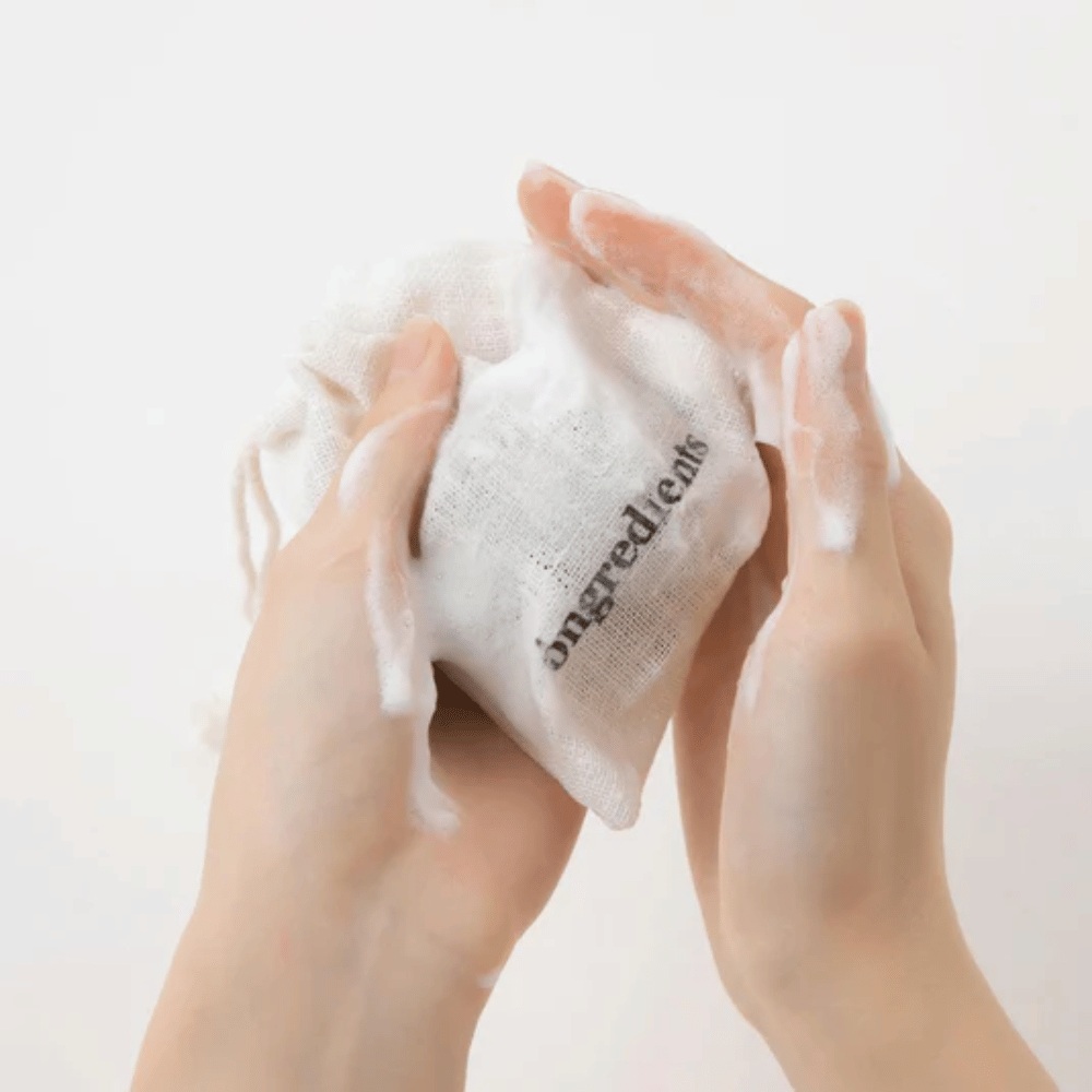 Mani che insaponano Óngredients Jeju Green Tea Cleansing Ball in una borsa di stoffa – vegano detergente viso con tè verde.