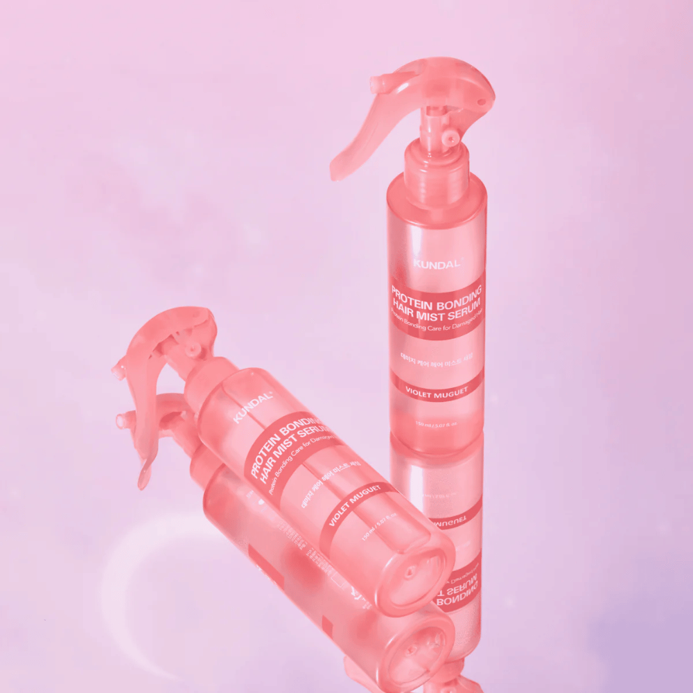 KUNDAL Protein Bonding Hair Mist Serum Violet Muguet in flaconi spray rosa, in piedi e sdraiati su uno sfondo rosa chiaro con riflesso.