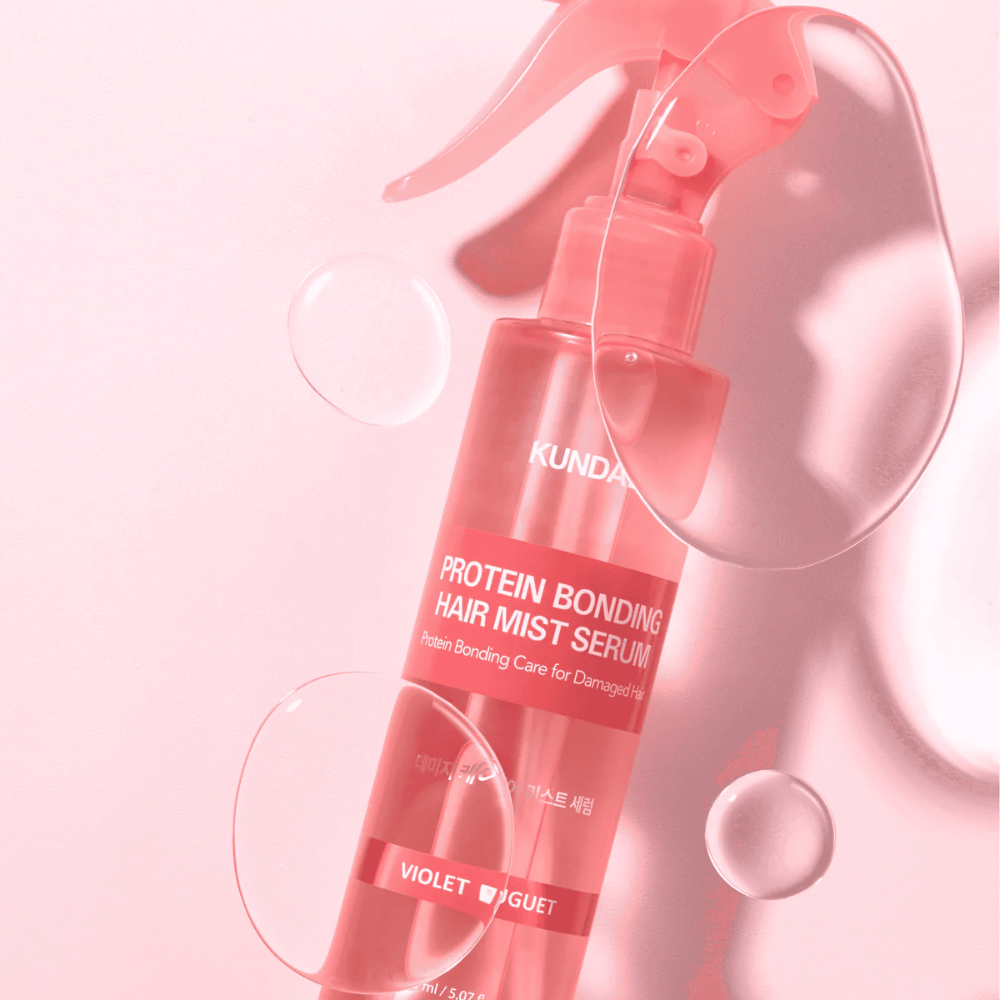 KUNDAL Protein Bonding Hair Mist Serum Violet Bouquet in flacone spray rosa, fotografato su sfondo rosa con gocce d'acqua.