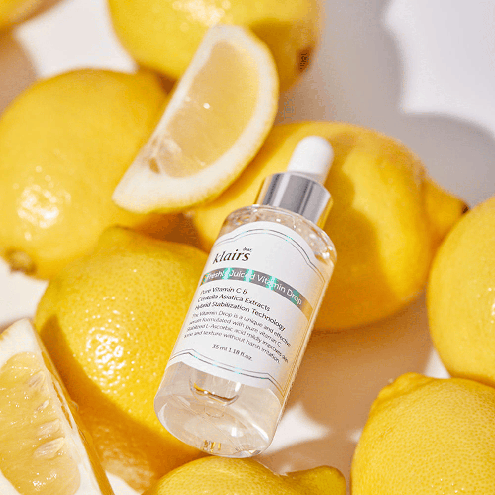 Klairs Freshly Juiced Vitamin Drop flacone di siero circondato da mezzi limoni freschi e fette di limone su una superficie chiara, mette in risalto gli ingredienti.