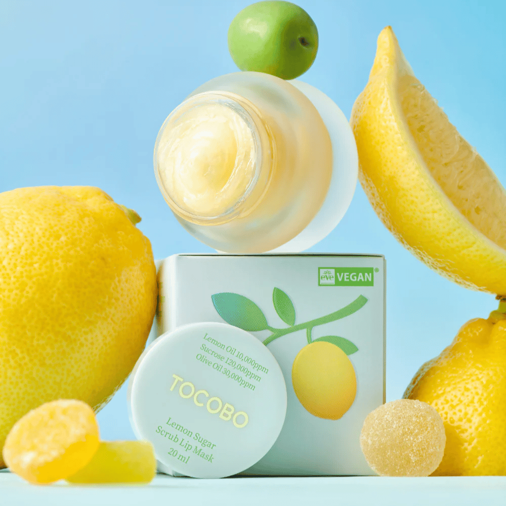 Barattolo con Tocobo Lemon Sugar Scrub Lip Mask posizionato tra limoni e confezione, contrassegnato come adatto ai vegani.