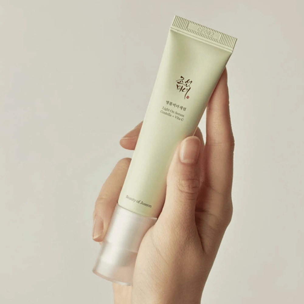 Una mano tiene Beauty of Joseon Light On Serum con Centella e vitamina C, in un tubo verde chiaro con design minimalista su uno sfondo neutro.
