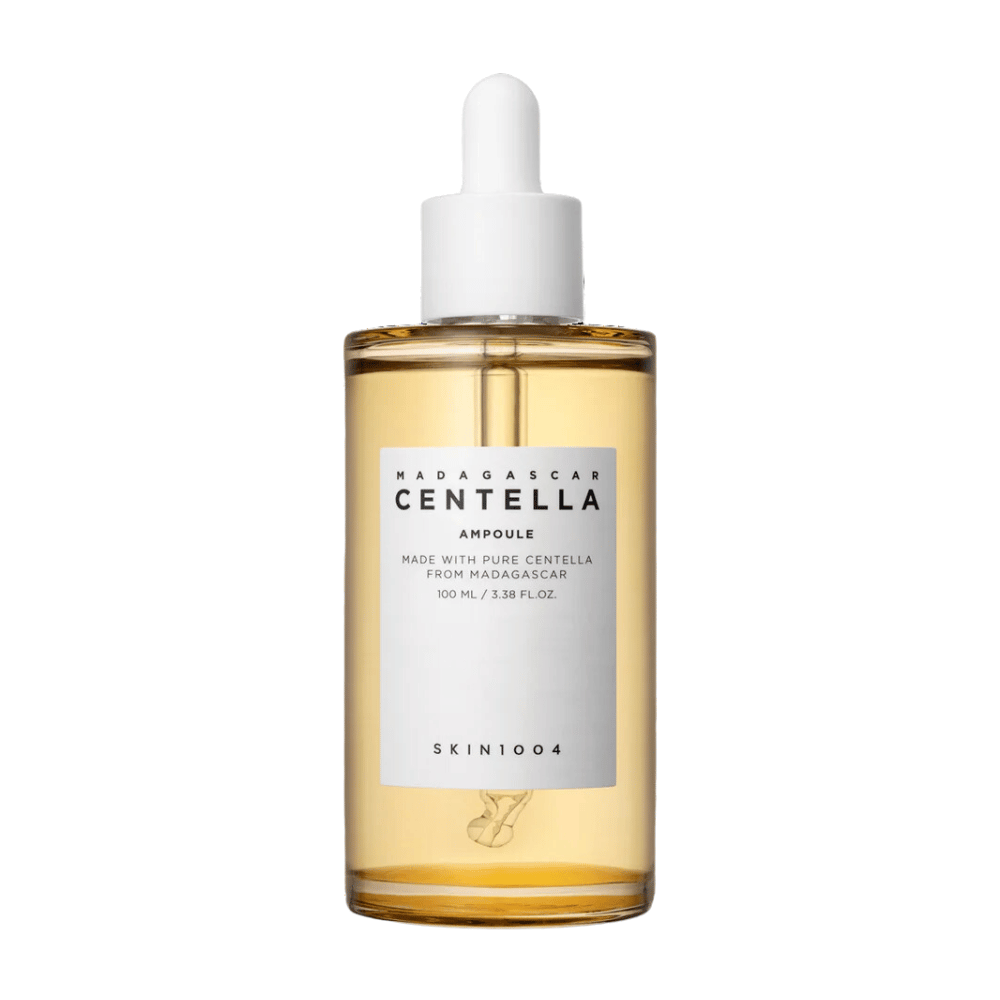 L'immagine mostra una bottiglia con "Madagascar Centella Asiatica 100 Ampoule" da SKIN1004. La bottiglia contiene 100 ml e sostiene di essere fatta con pura Centella del Madagascar. Il prodotto sembra essere un siero per la cura della pelle e l'etichetta semplice dà un'impressione di purezza e naturalità. La bottiglia con tappo contagocce suggerisce che si tratta di un prodotto per la cura della pelle dosato con attenzione.