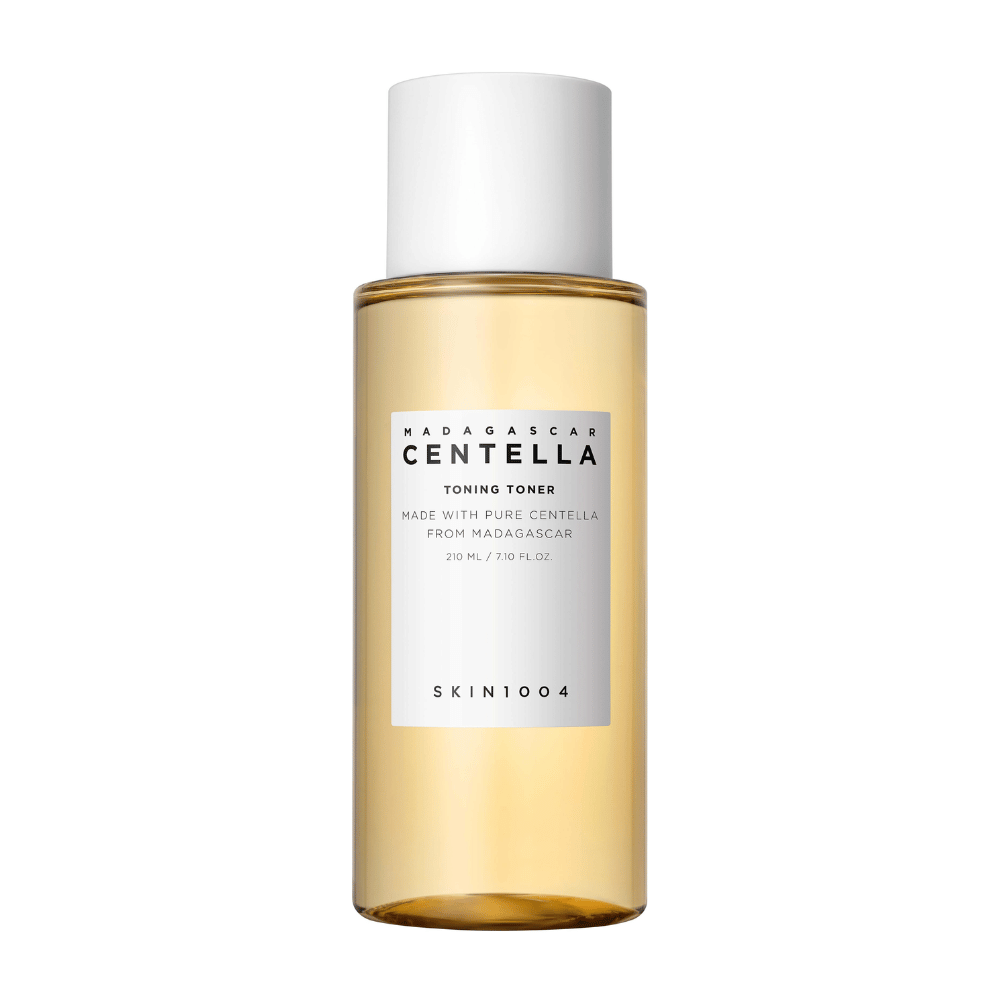 L'immagine mostra una bottiglia con tonalità per la cura della pelle, etichettata "Madagascar Centella Toning Toner" da SKIN1004. Il prodotto è indicato come contenente 210 ml o 7.10 fl.oz ed è realizzato con pura Centella del Madagascar. La confezione è semplice ed elegante con una bottiglia trasparente e un liquido dorato tonico viso all'interno, che conferisce una sensazione di lusso e purezza. Il logo del marchio SKIN1004 è chiaramente visibile nella parte inferiore dell'etichetta.
