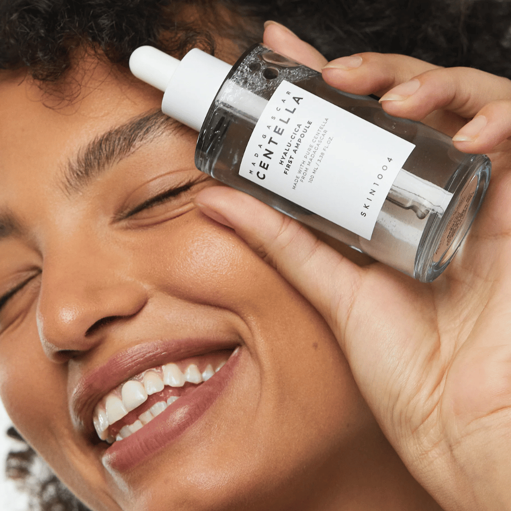 Donna sorridente tiene Skin1004 Madagascar Centella Hyalu-Cica First Ampoule accanto al viso.