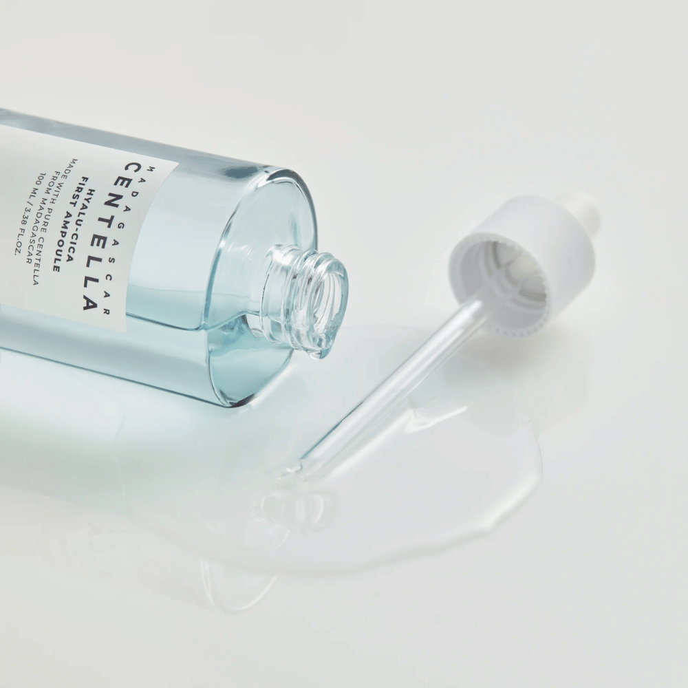 Primo piano di una bottiglia aperta Skin1004 Madagascar Centella Hyalu-Cica First Ampoule con pipetta sdraiata e siero sparso su superficie bianca.