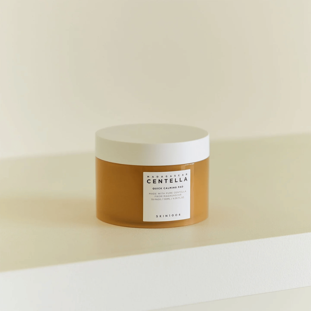 SKIN1004 Madagascar Centella Quick Calming Pad posizionato su uno scaffale bianco – barattolo color ambra con coperchio bianco ed etichetta evidente sul davanti.