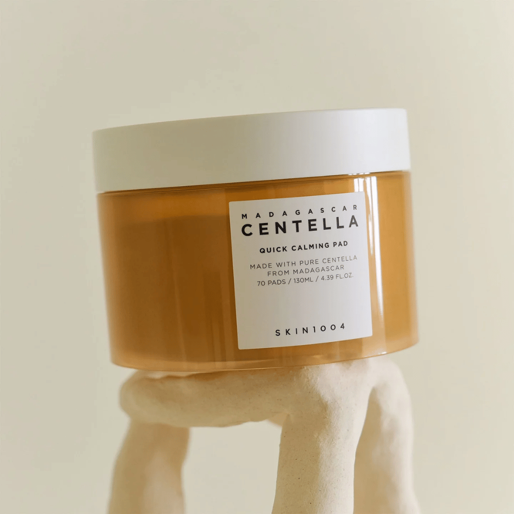 Barattolo con SKIN1004 Madagascar Centella Quick Calming Pad posizionato su un piedistallo bianco simile a una scultura – contenitore color ambra con etichetta e coperchio bianchi.