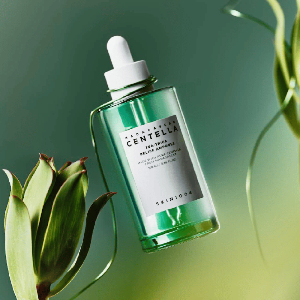 SKIN1004 Madagascar Centella Tea-Trica Relief Ampoule – bottiglia di vetro verde con pipetta, etichetta bianca e contenuto di 100 ml, fotografata su sfondo verde con dettagli vegetali.