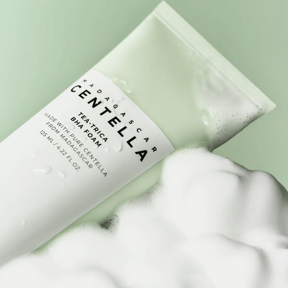 Un prodotto del tipo schiuma detergente, "Madagascar Centella Tea-trica BHA Foam", è parzialmente visibile con schiuma intorno. Il prodotto ha un design verde e bianco, e il testo "Madagascar Centella" e "Tea-trica BHA Foam" sono chiaramente visibili. Il volume è di 125 ml.