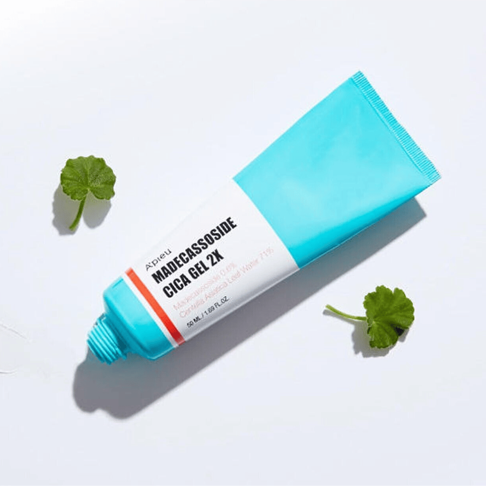 A'pieu Madecassoside Cica Gel 2X in un tubo blu con etichetta bianca, circondato da tre foglie di centella asiatica verdi su sfondo bianco.