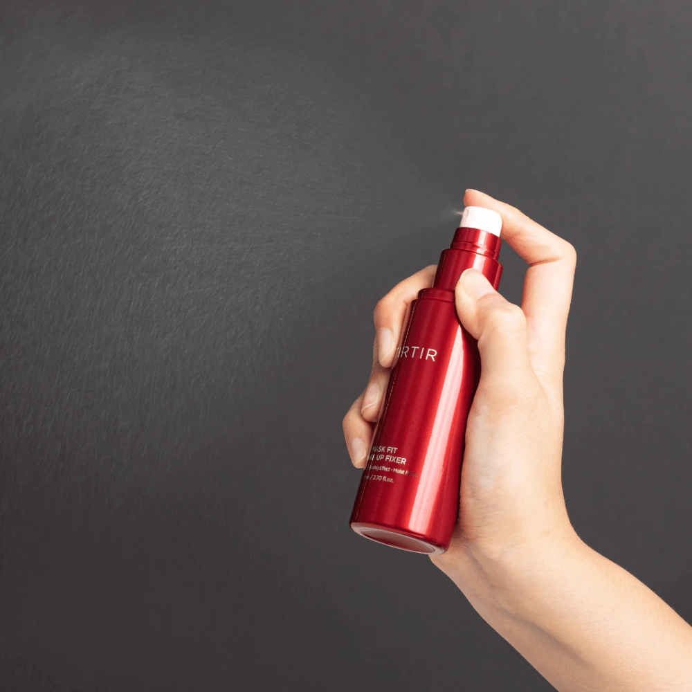 Una mano che tiene una bottiglia rossa del marchio tirtir Mask Fit Make Up Fixer e spruzza una fine nebbia, ideale per fissare il trucco.