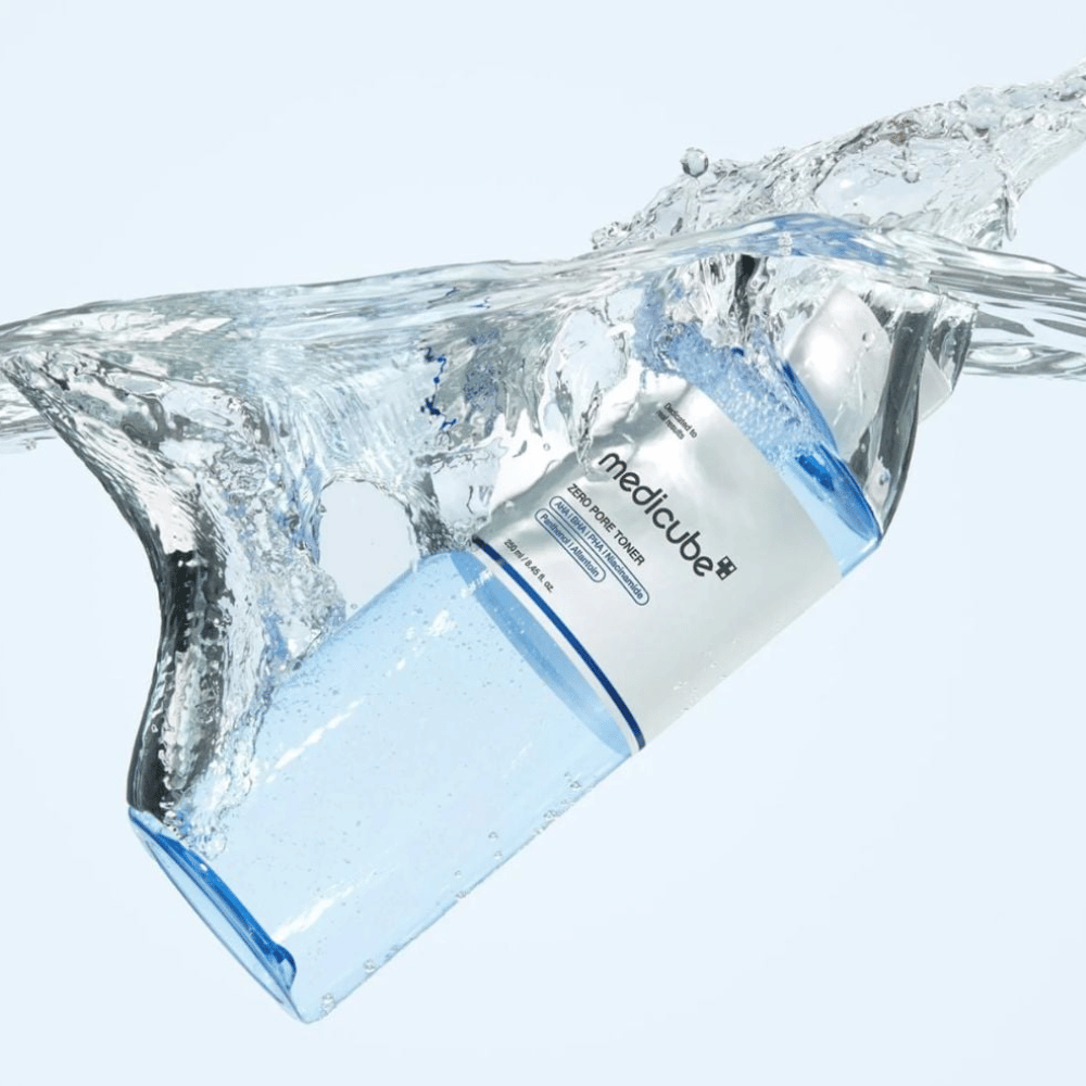 Medicube Zero Pore Toner 250 ml, tonico esfoliante con AHA, BHA e PHA. Bottiglia blu trasparente circondata da un grande spruzzo d'acqua.