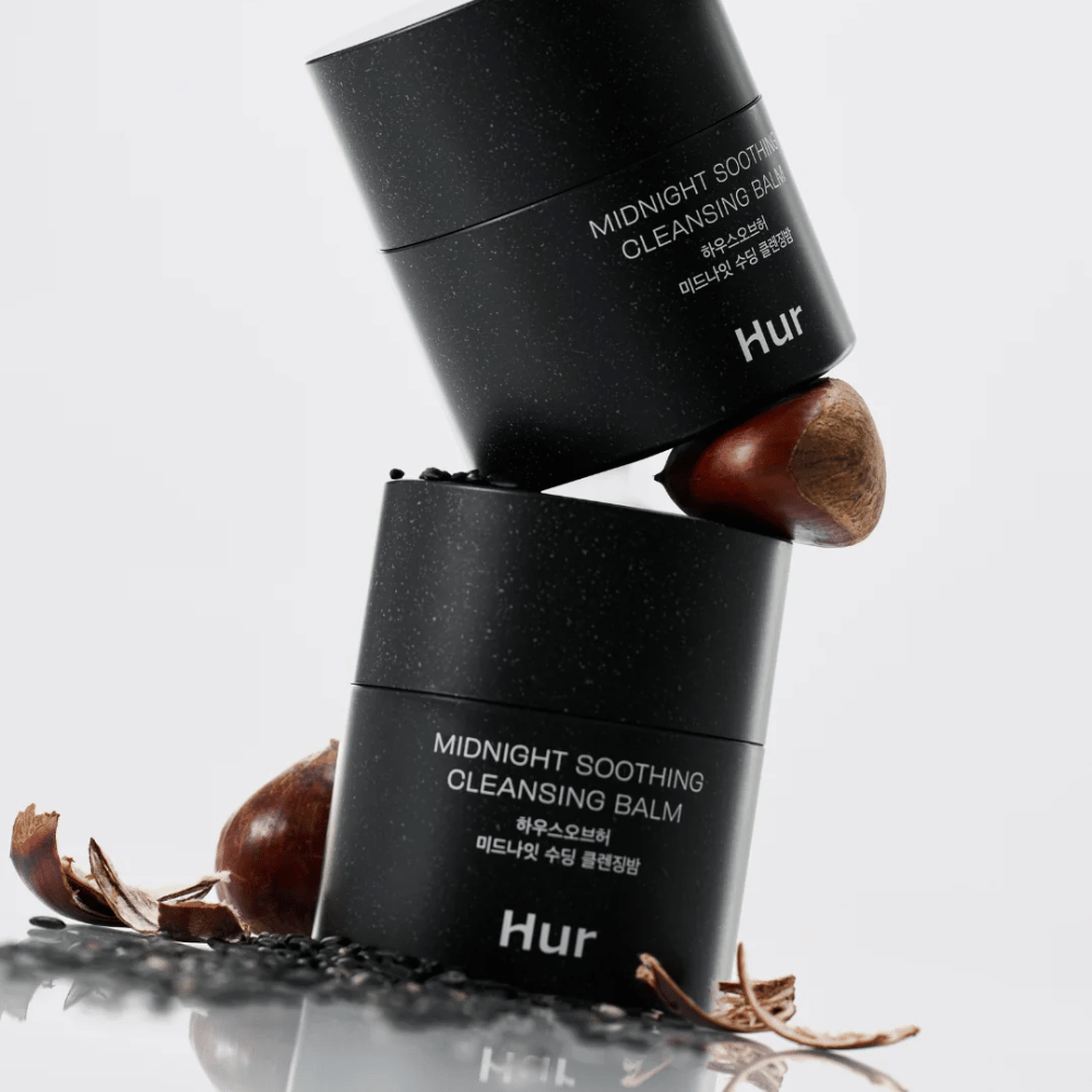 Due barattoli di Come Midnight Soothing Cleansing Balm impilati con ingredienti naturali. Balsamo detergente nutriente per la pulizia quotidiana della pelle sensibile.