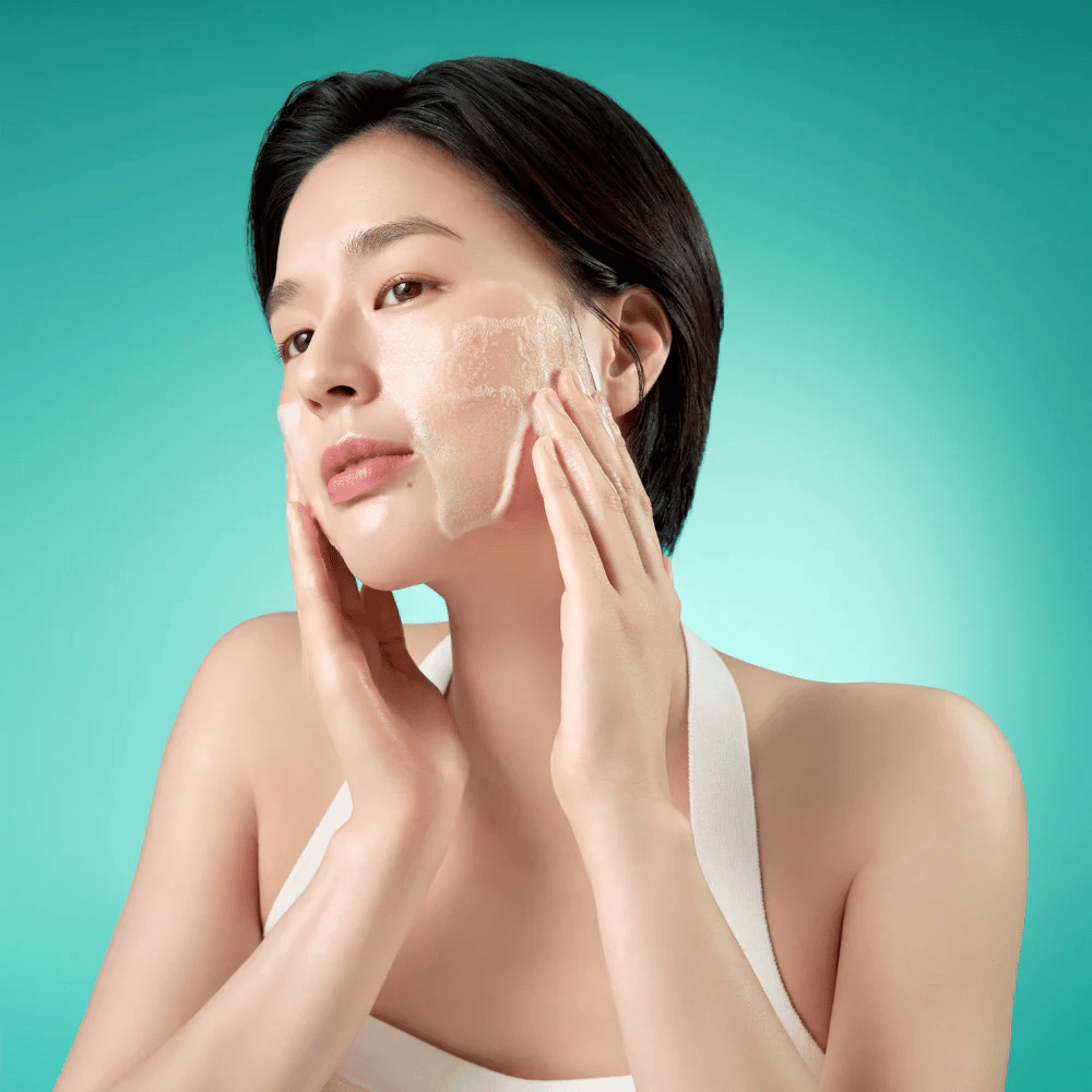 Donna che pulisce il viso con una schiuma detergente delicata su sfondo verde.