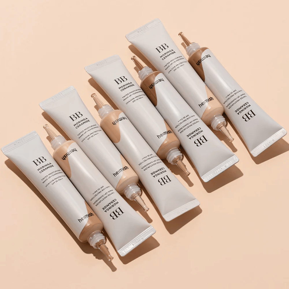 Diversi tubetti di Heimish Moringa Ceramide BB Cream disposti su uno sfondo beige chiaro. L'immagine evidenzia le diverse tonalità e l'elegante design minimalista della confezione del prodotto.