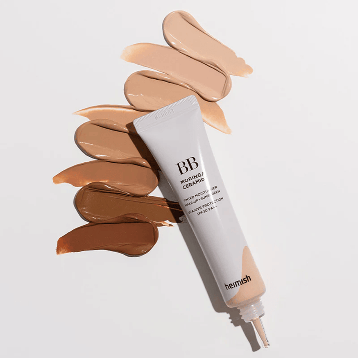 Heimish Moringa Ceramide BB Cream circondato da diversi campioni di tonalità in vari incarnati. L'immagine mostra l'ampia gamma di colori del prodotto e la consistenza cremosa che offre una copertura naturale e un incarnato uniforme.