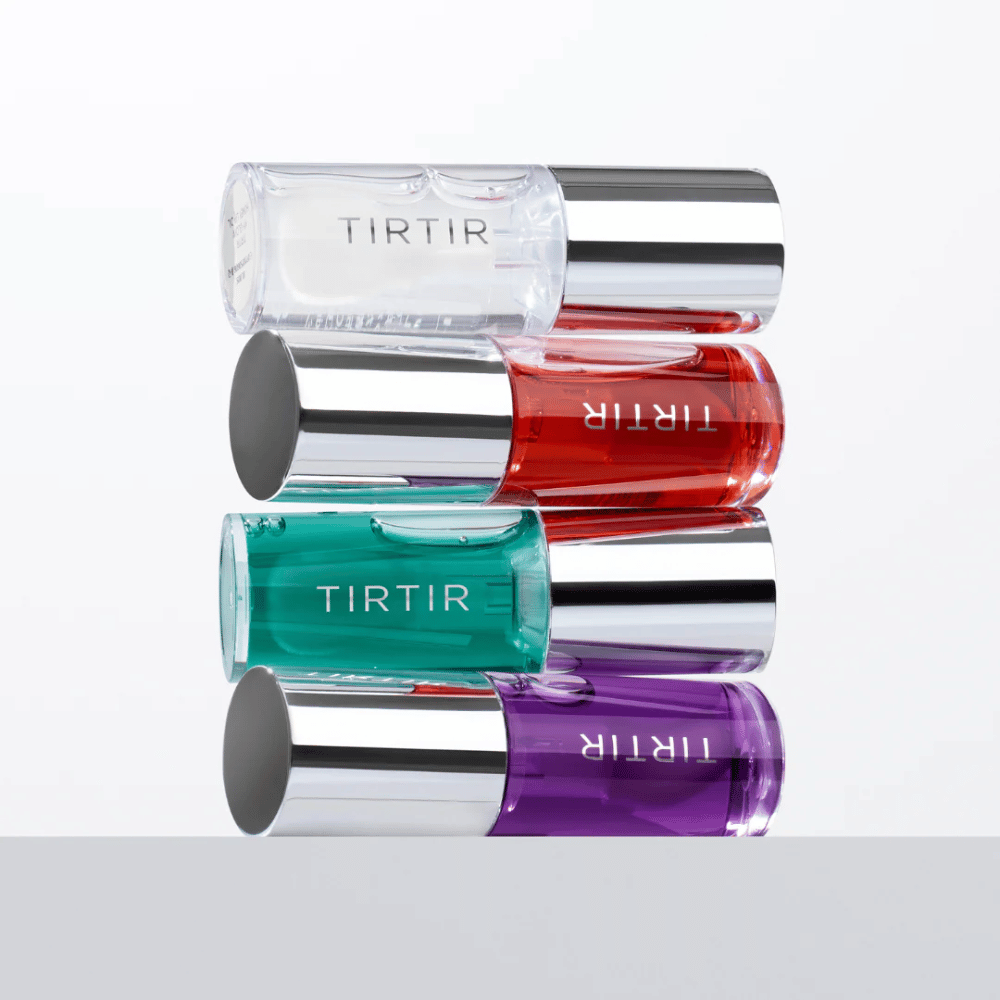 Quattro TIRTIR My Glow Lip Oil in diversi colori – trasparente, rosso, verde e viola – impilati uno sopra l'altro con coperchi argentati su sfondo bianco.