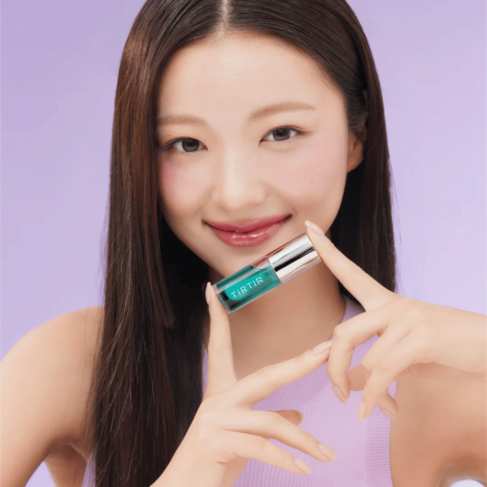 Donna con capelli lunghi e lisci tiene in mano TIRTIR My Glow Lip Oil e mostra le sue labbra lucide e rosa su uno sfondo viola.